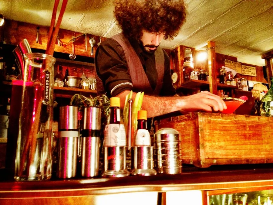 A bartender garnishing a cocktail behind the bar at The Old School Yard